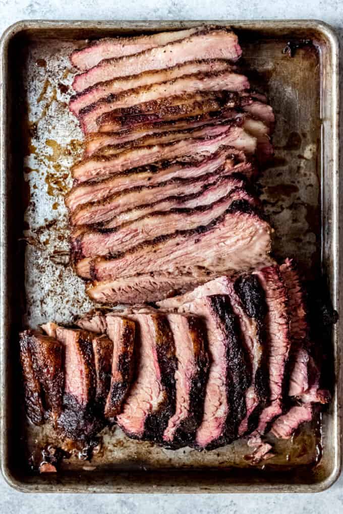 An image of sliced smoked brisket on a baking sheet.