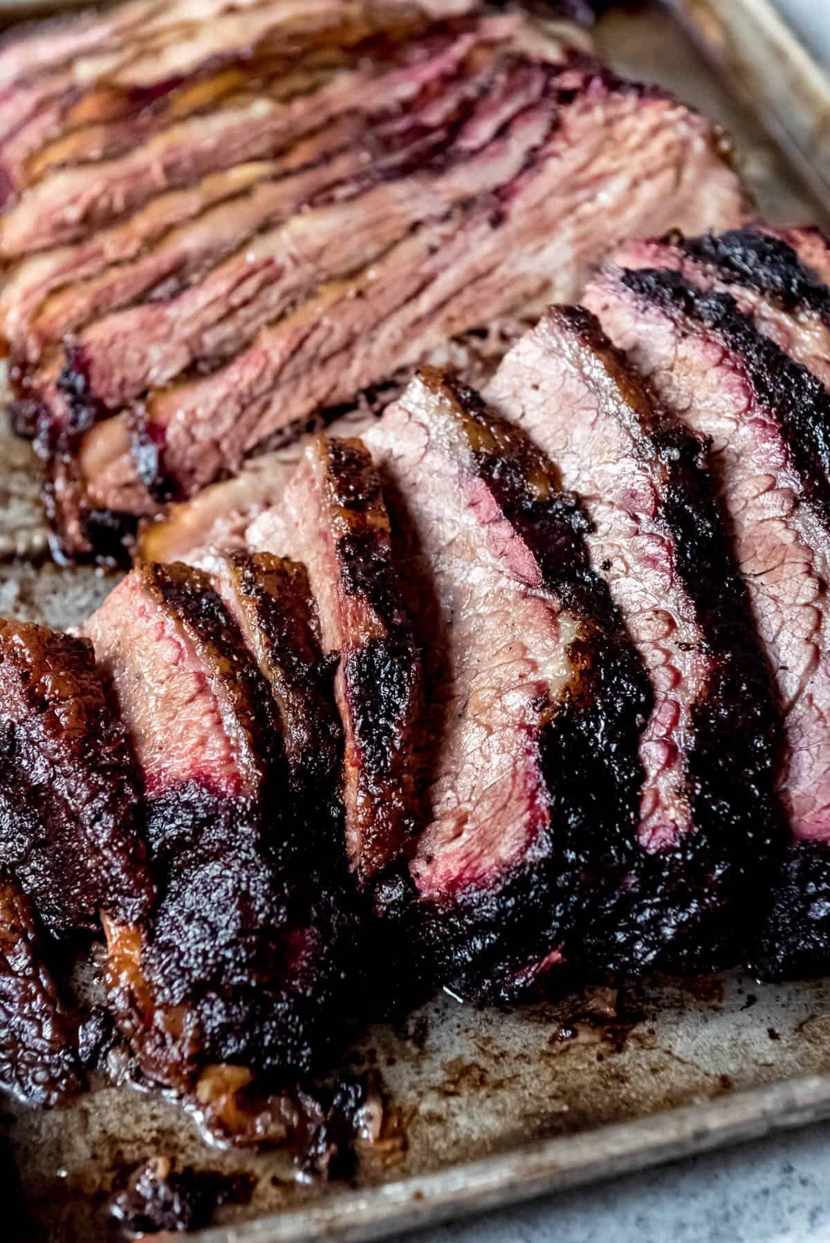 An image of tender, juicy slices of smoked brisket with a smoke ring and dark crusty bark around the edges.