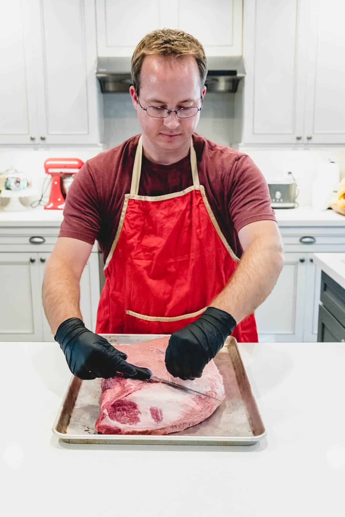 An image of a man in a red apron trimming the fat cap of a beef brisket.