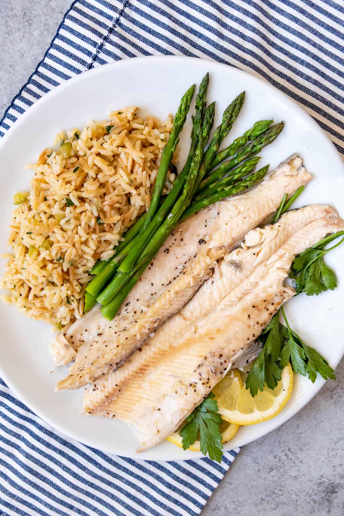 An image of baked rainbow trout fillets on a plate with homemade rice pilaf and roasted asparagus.