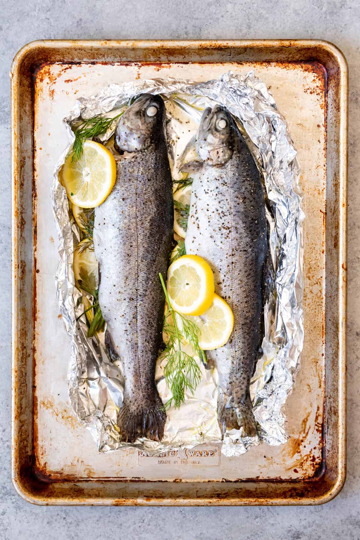 An image of two whole rainbow trout on foil with sliced lemon and herbs.