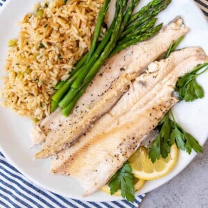 Grilled trout on a plate with rice and asparagus.