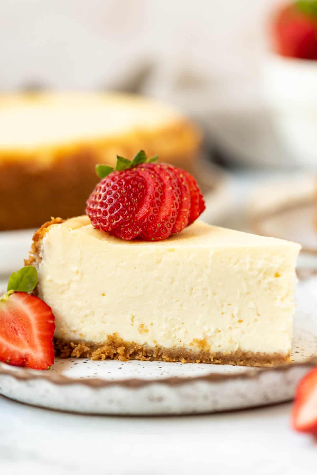 Close up of a slice of cheesecake with a sliced strawberry on top.