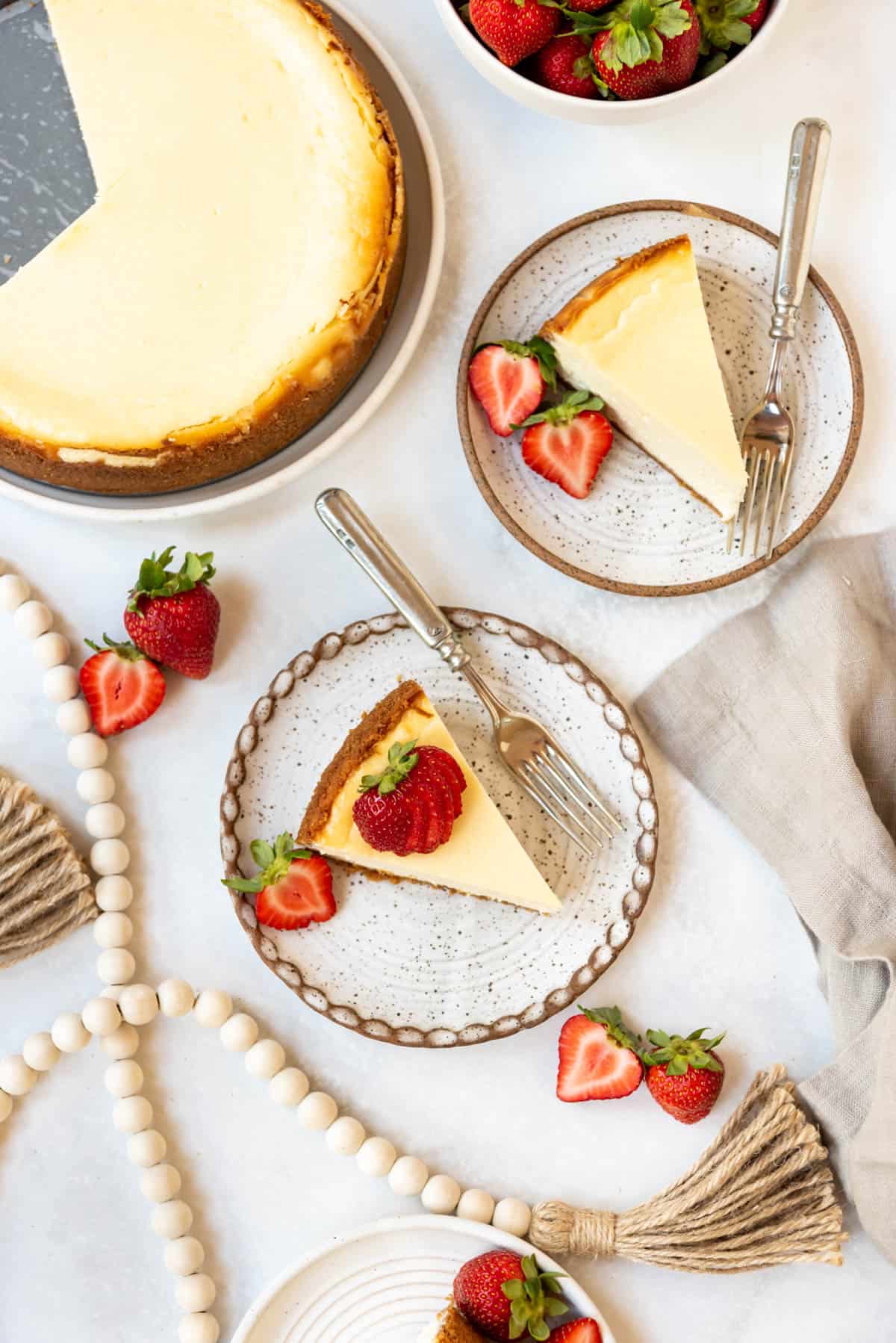 Top view of cheesecake with sliced strawberries on top, laid out on a table on plates with cutlery. 