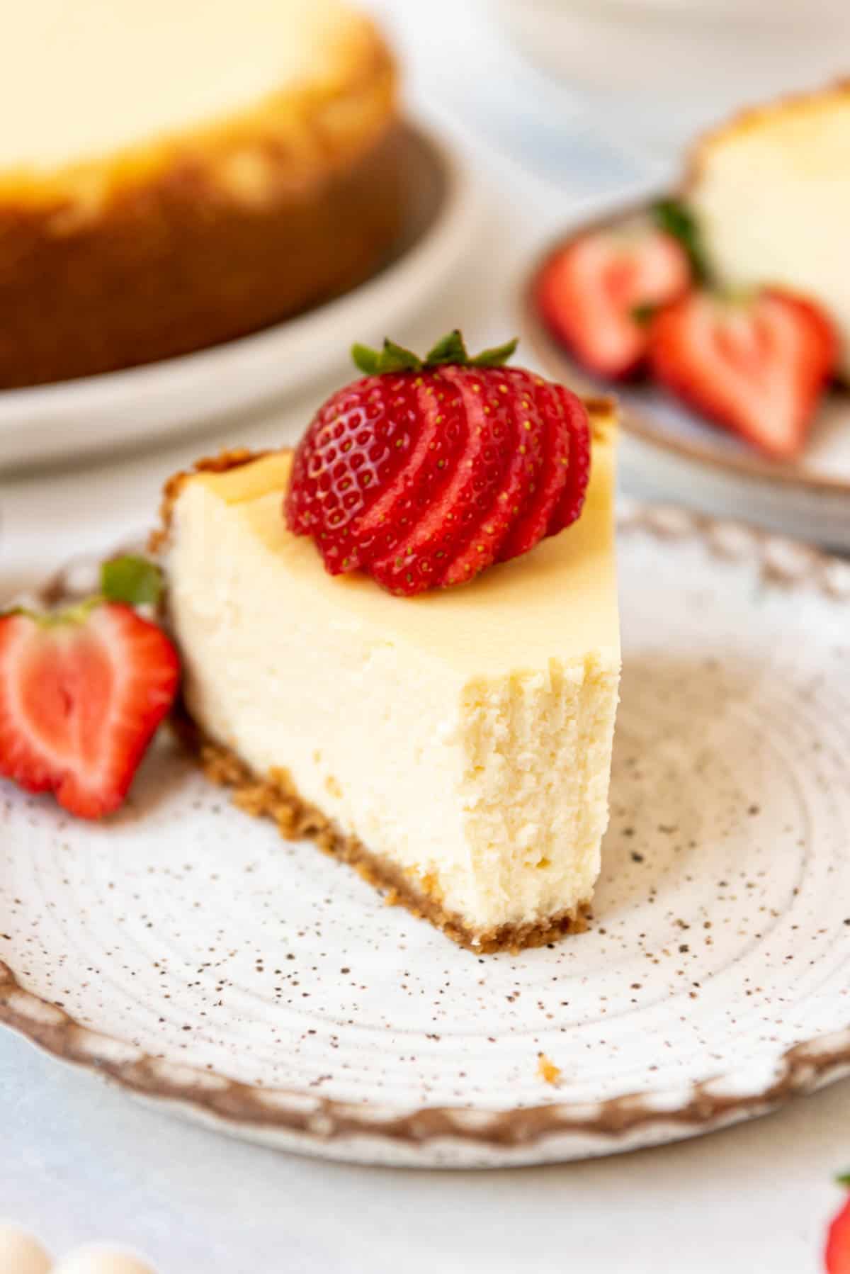 Close up of a slice of cheesecake on a plate, topped with sliced strawberries with a bite taken out of it. 