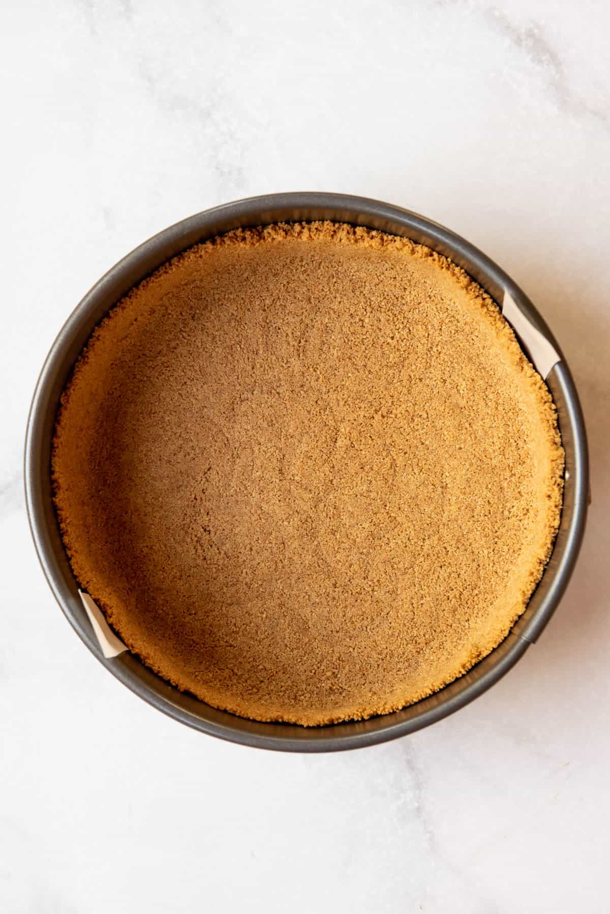Top view of a cheesecake pan with crushed graham crackers pressed into the bottom of the pan. 