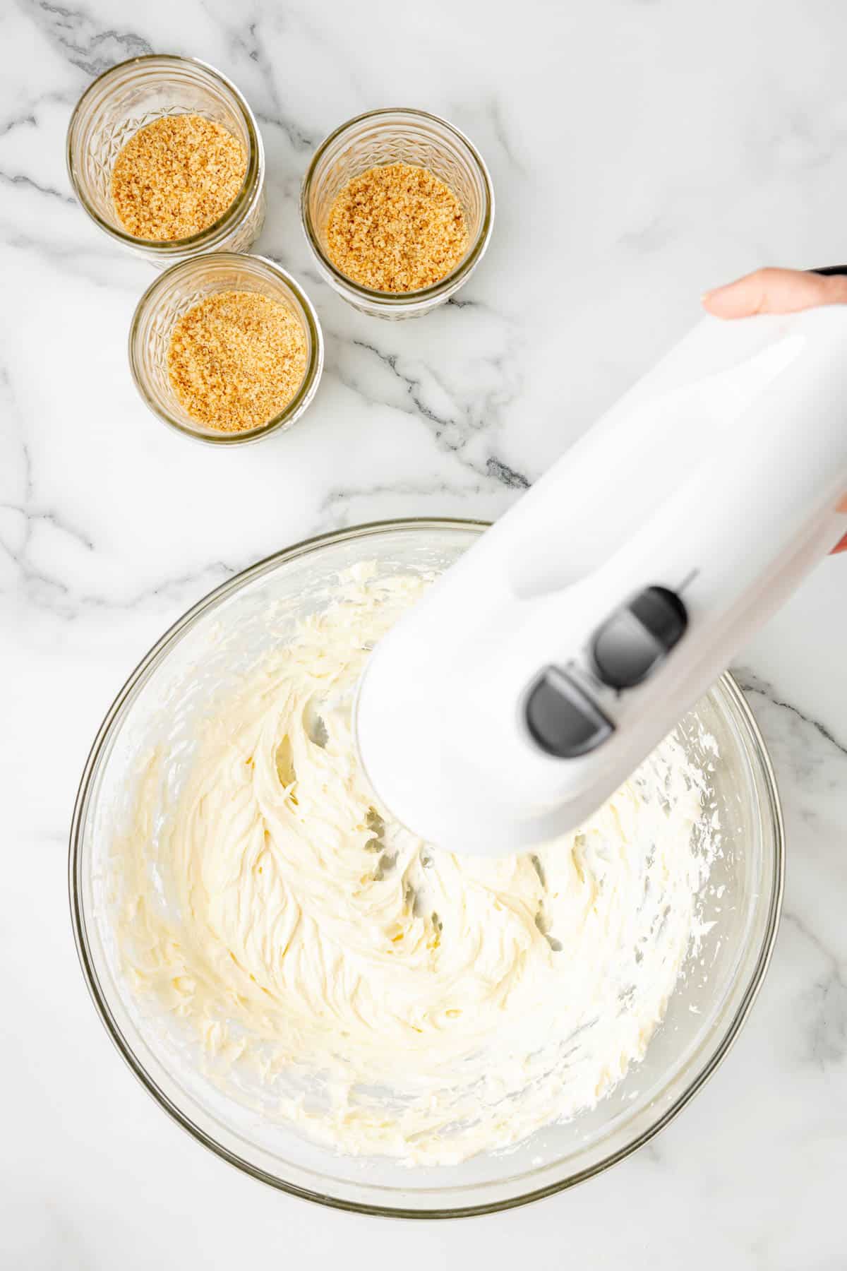 An electric mixer being used to beat cream cheese and sugar until smooth.