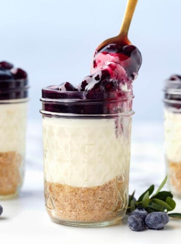 A spoonful of no-bake cheesecake with blueberry topping being lifted from a jar.