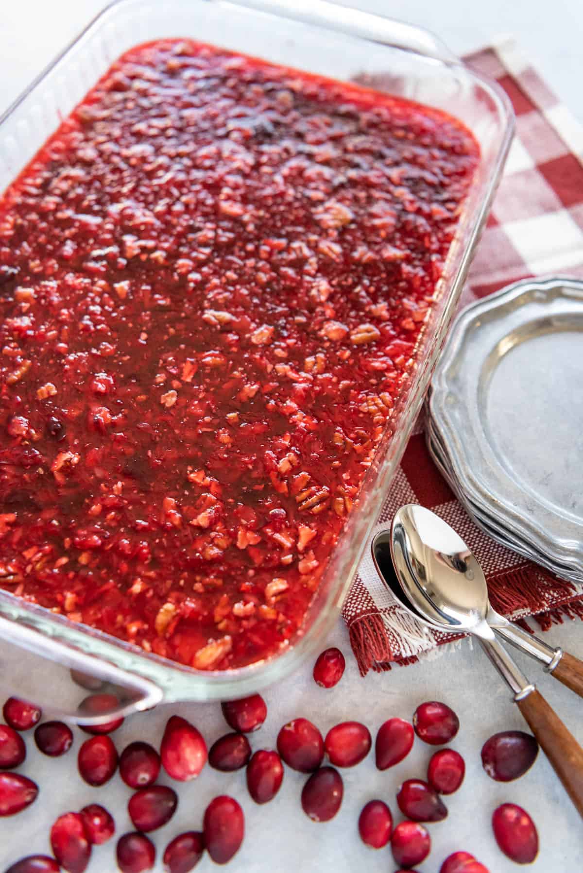 Cranberry jello salad in baking dish with fresh cranberries spoons and plates to the sides.