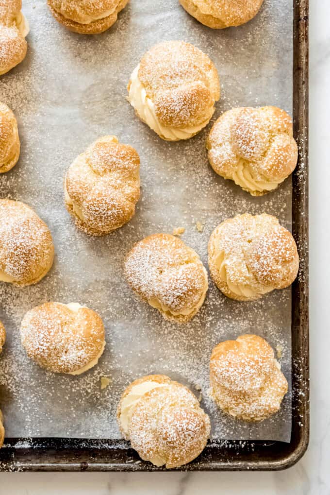 An image of filled cream puffs on a baking sheet and dusted with powdered sugar.