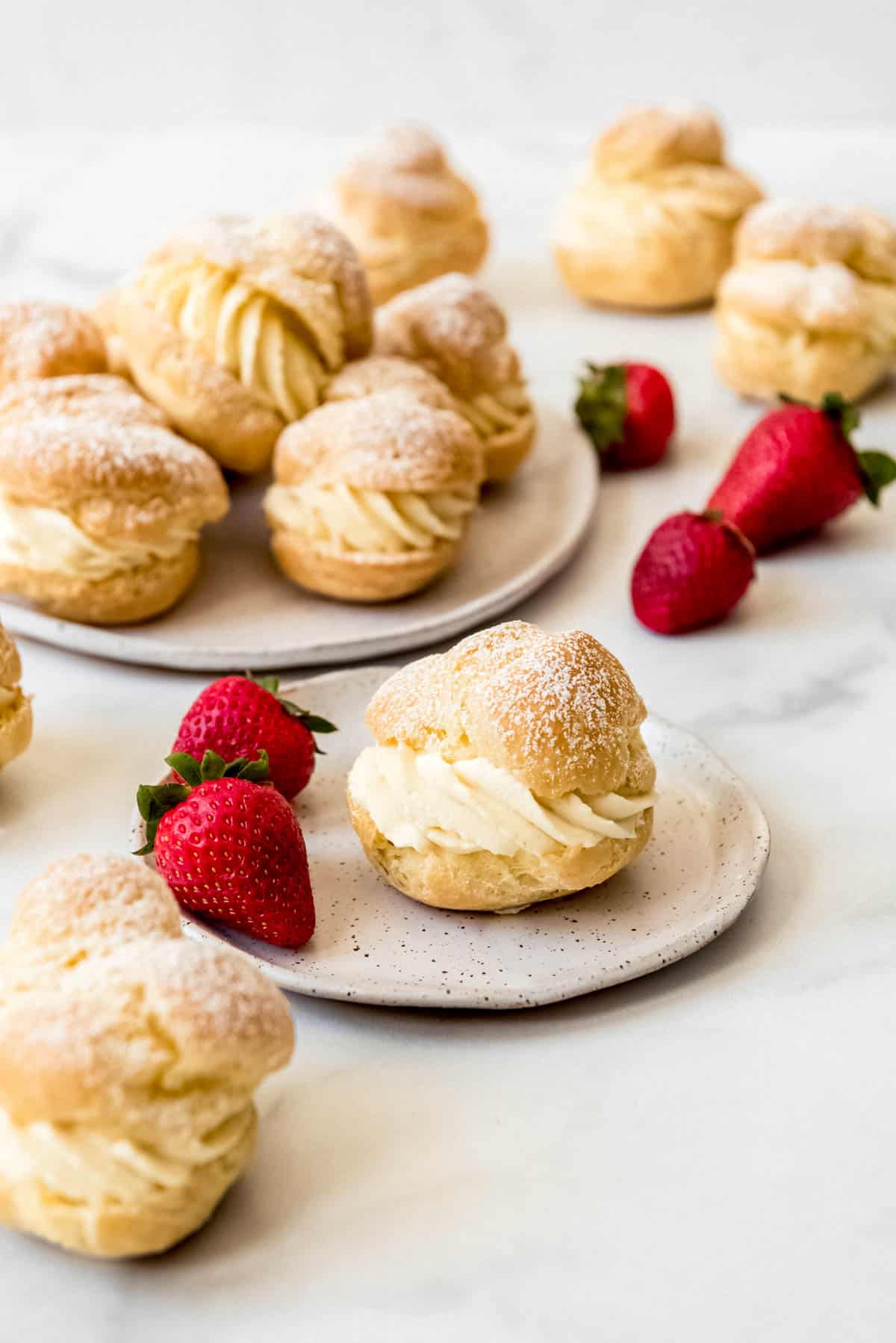 A cream puff on a plate with two strawberries next to more cream puffs.