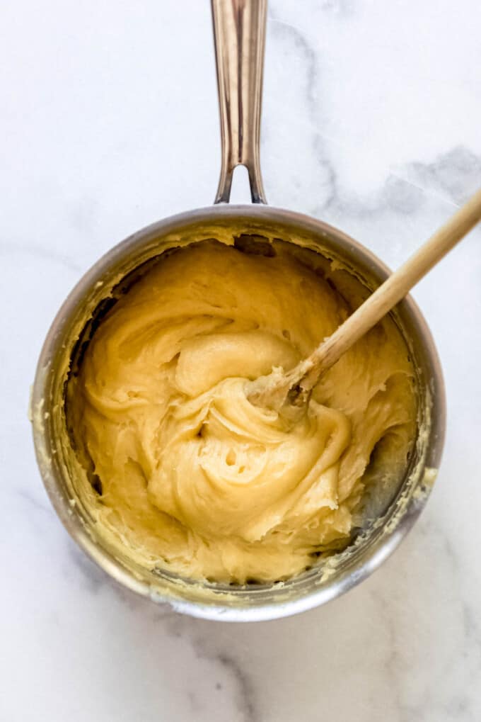Cream puff batter in a saucepan with a wooden spoon.