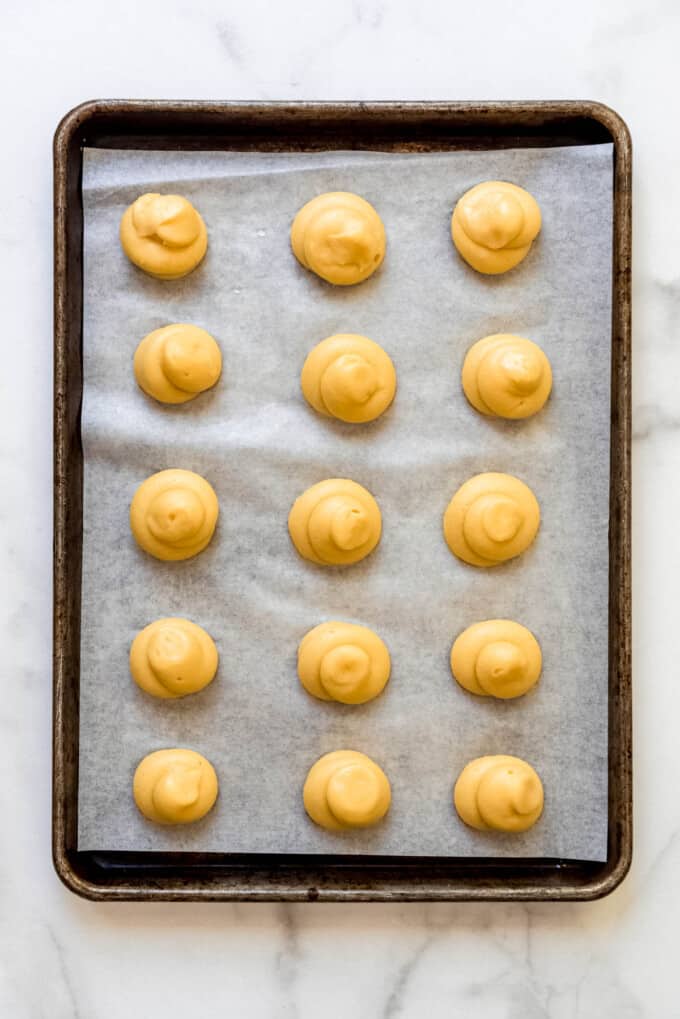 An image of cream puff batter on a parchment lined baking sheet getting ready to be baked.