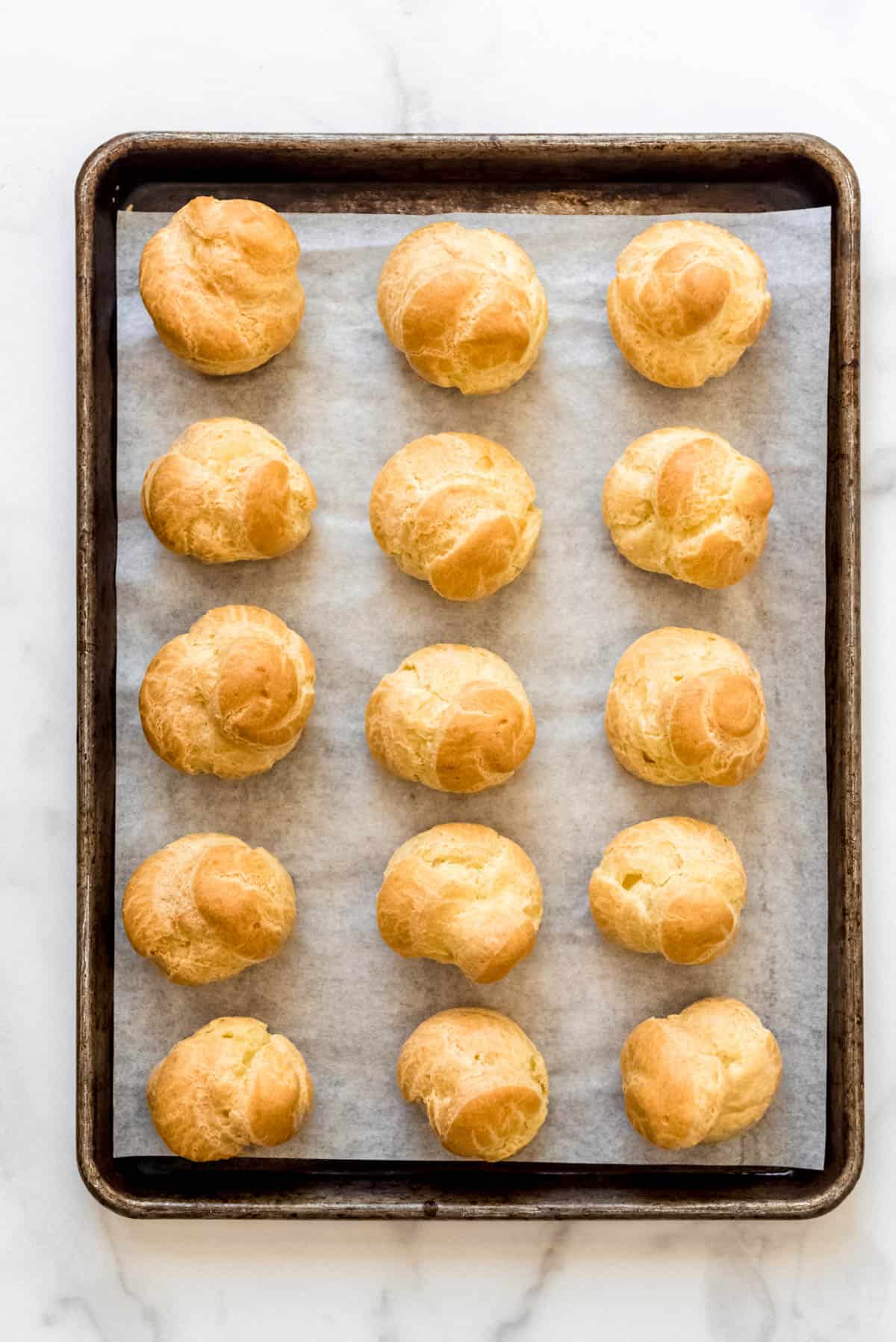 Baked cream puffs on a parchment lined baking sheet.