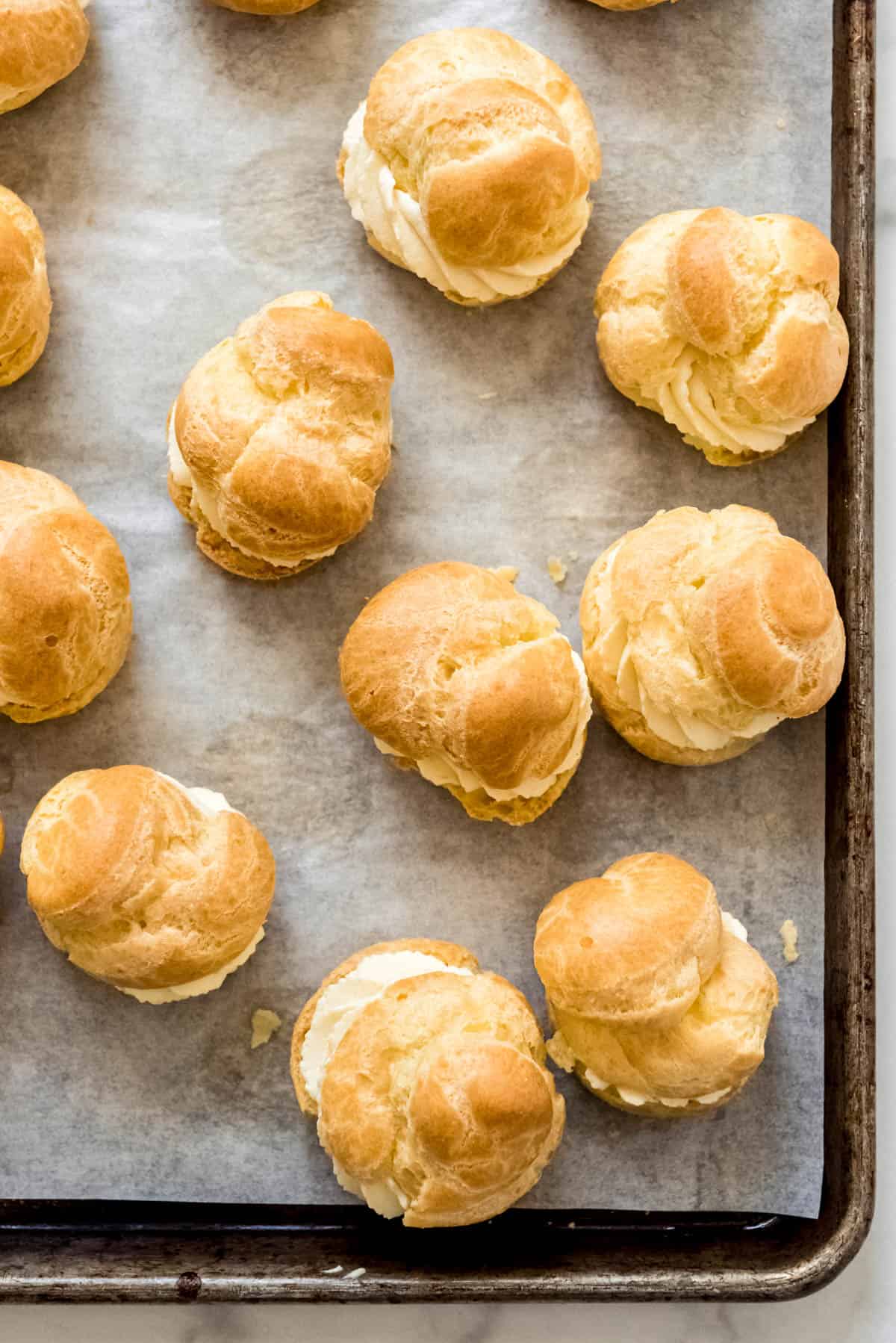 An image of plain filled cream puffs on a baking sheet.