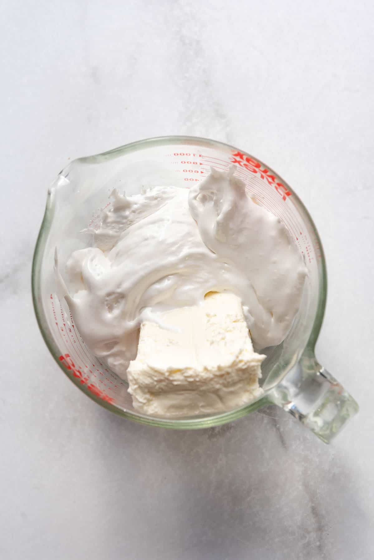 Marshmallow fluff and cream cheese in a glass mixing bowl.