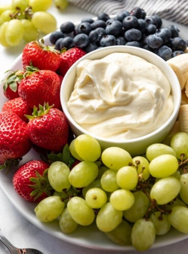Close up of fresh fruit dip in a small bowl surrounded by berries and grapes on a fruit platter.
