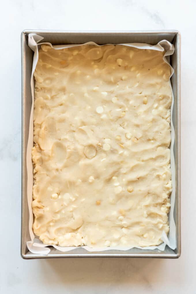 Shortbread dough with macadamia nuts and white chocolate chips pressed into a baking pan.