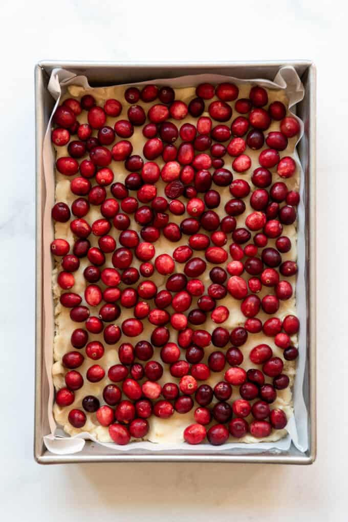 Adding fresh cranberries on top of shortbread dough in a baking pan.