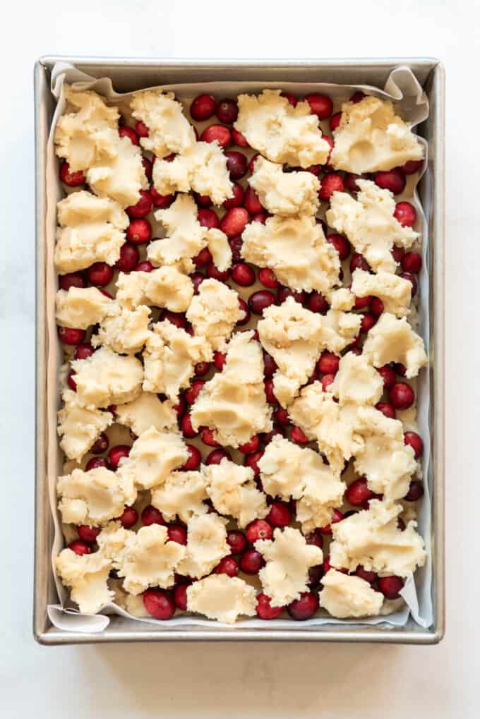 Scattering shortbread dough over fresh cranberries in a baking pan.