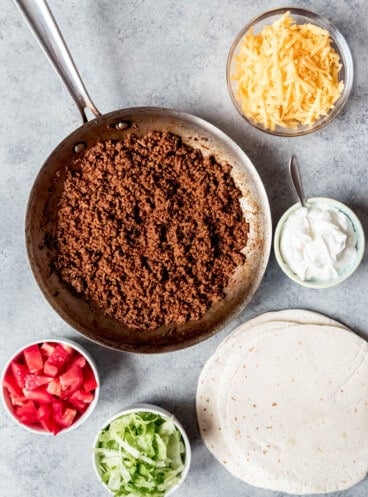 An image of ground beef seasoned taco filling with taco fixings next to it.