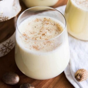A Glass of homemade eggnog on a table with nuts around it.