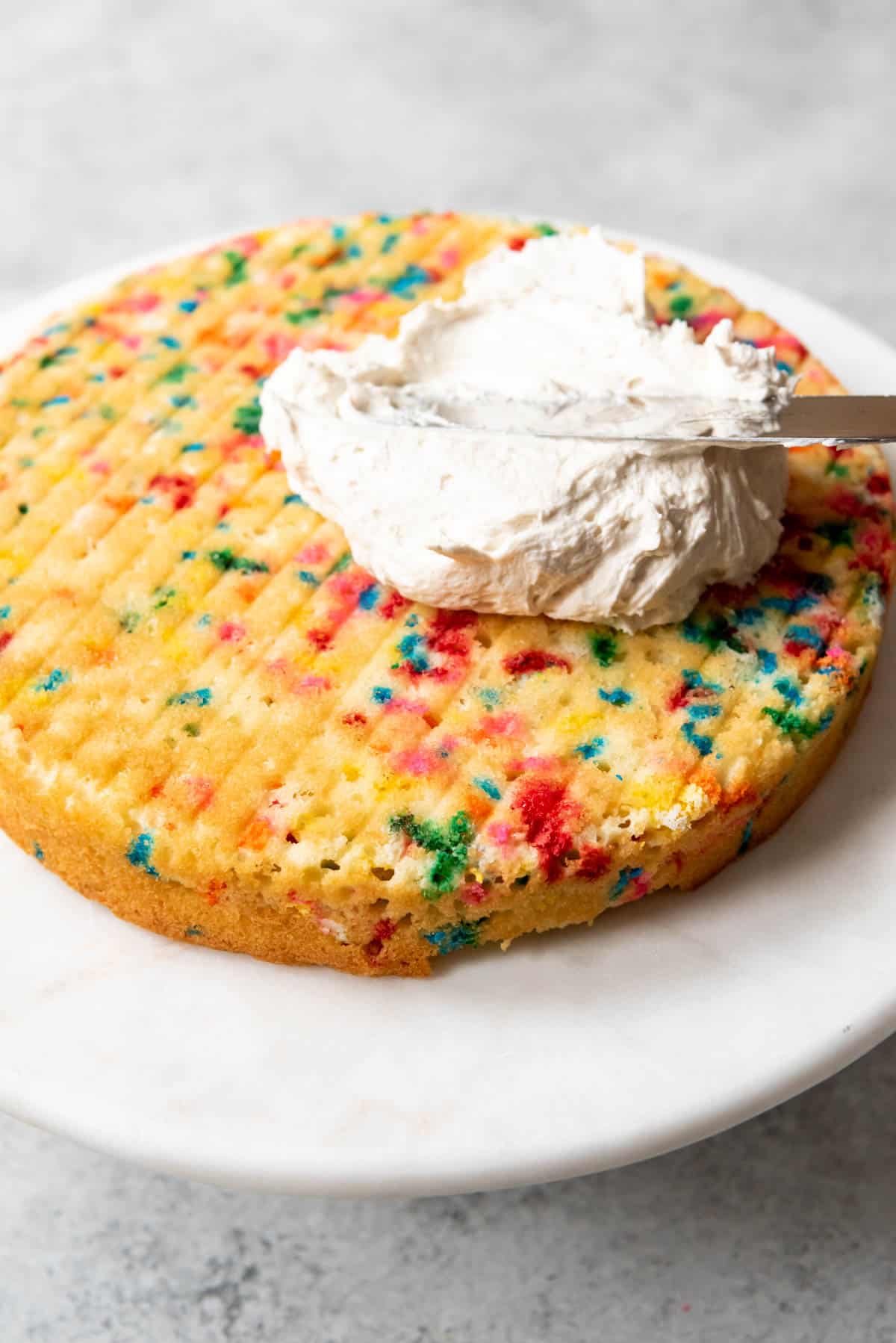 An image of Homemade funfetti round cake with a scoop of frosting on it ready to be spread.