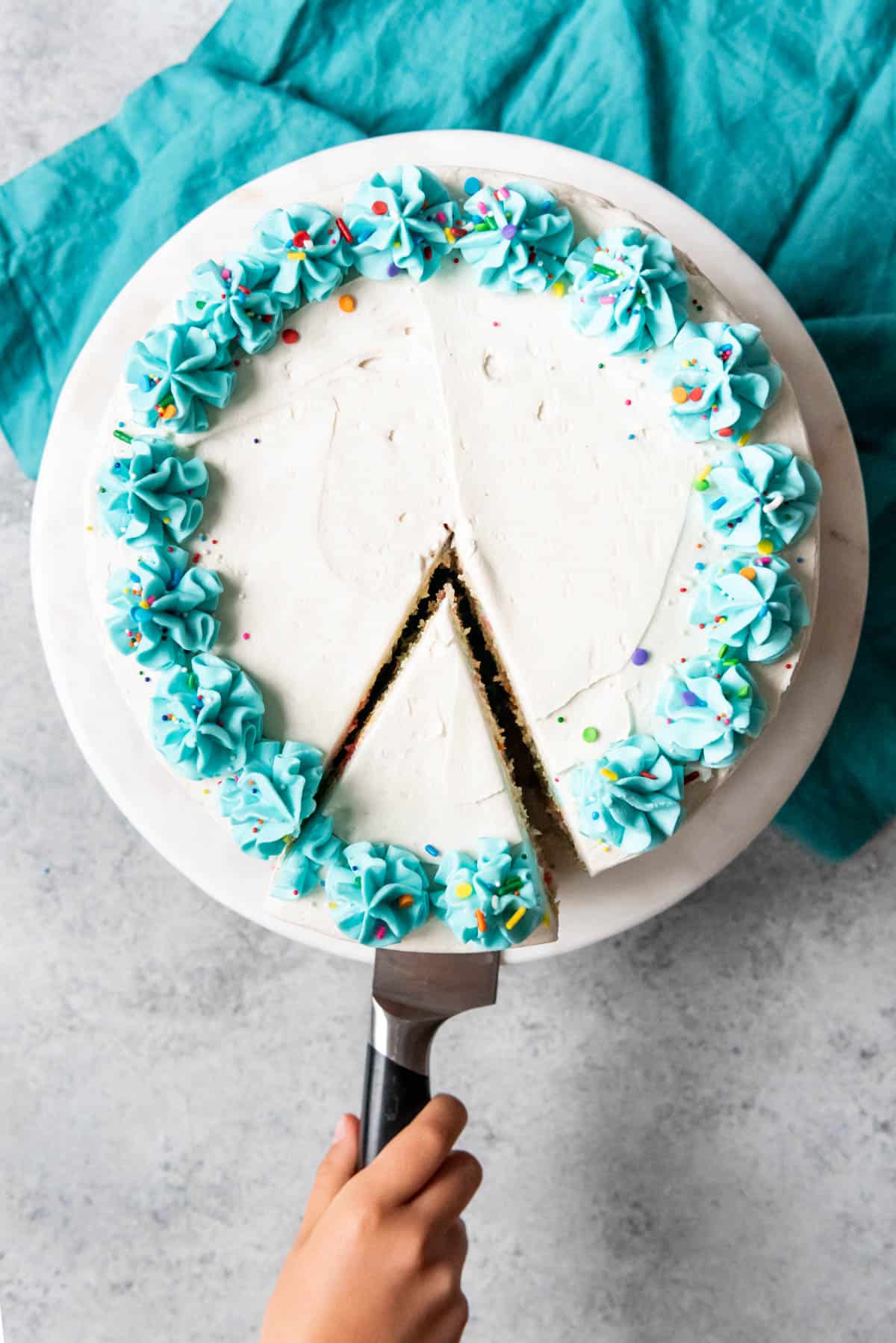 An image of one slice of homemade confetti cake being removed from the cake plate.