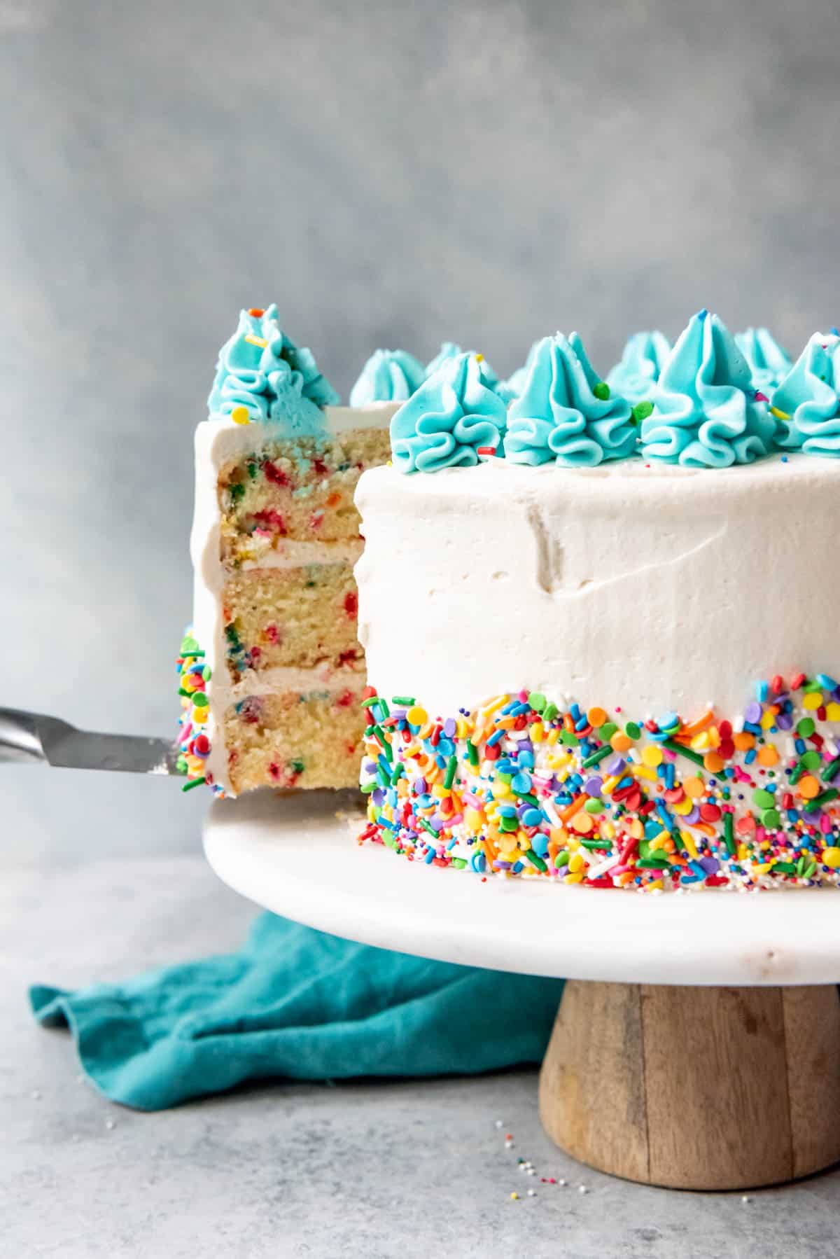 An image of a sprinkle cake with a slice being lifted out of it from the cake stand.