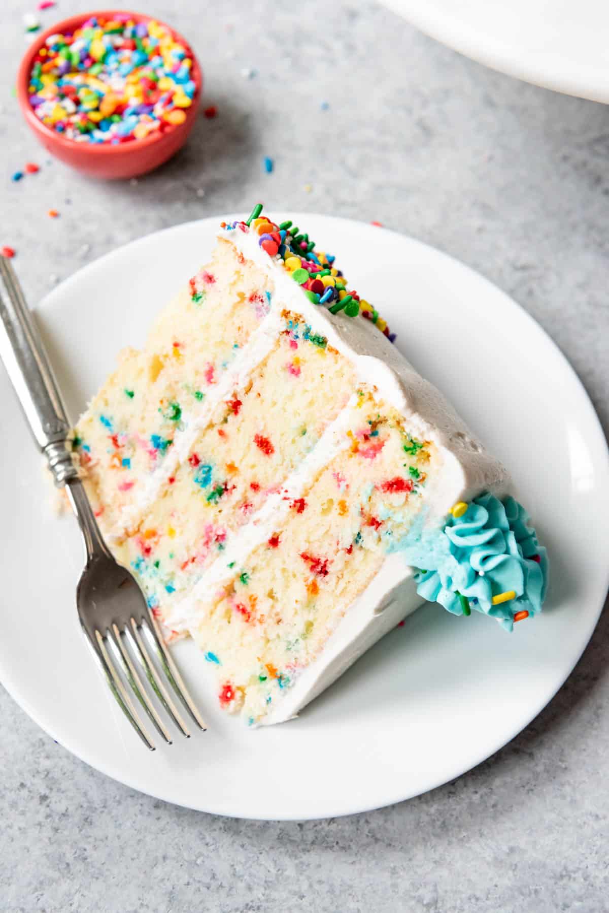 A slice of homemade funfetti cake laying on a white plate.