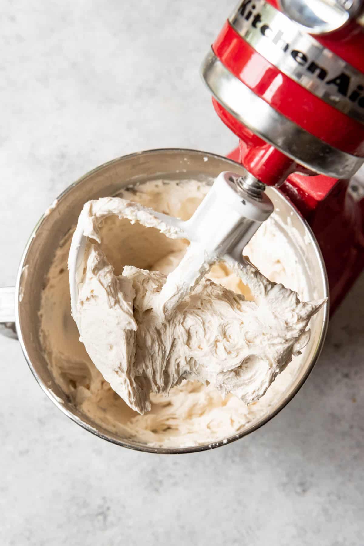 An image of Buttercream frosting getting mixed in a red kitchen aid stand up mixer.