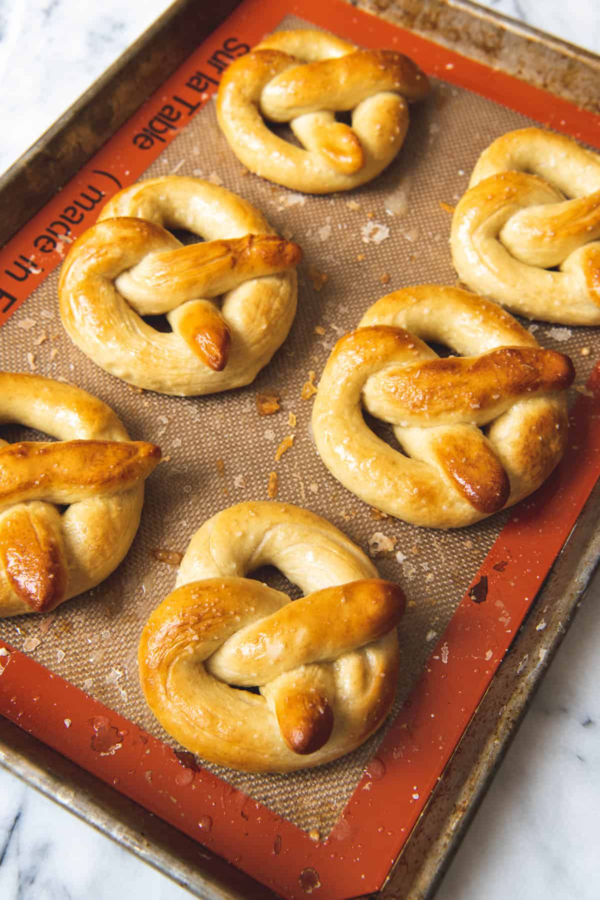 An image of golden brown homemade soft pretzels on a baking sheet with a silicon mat.