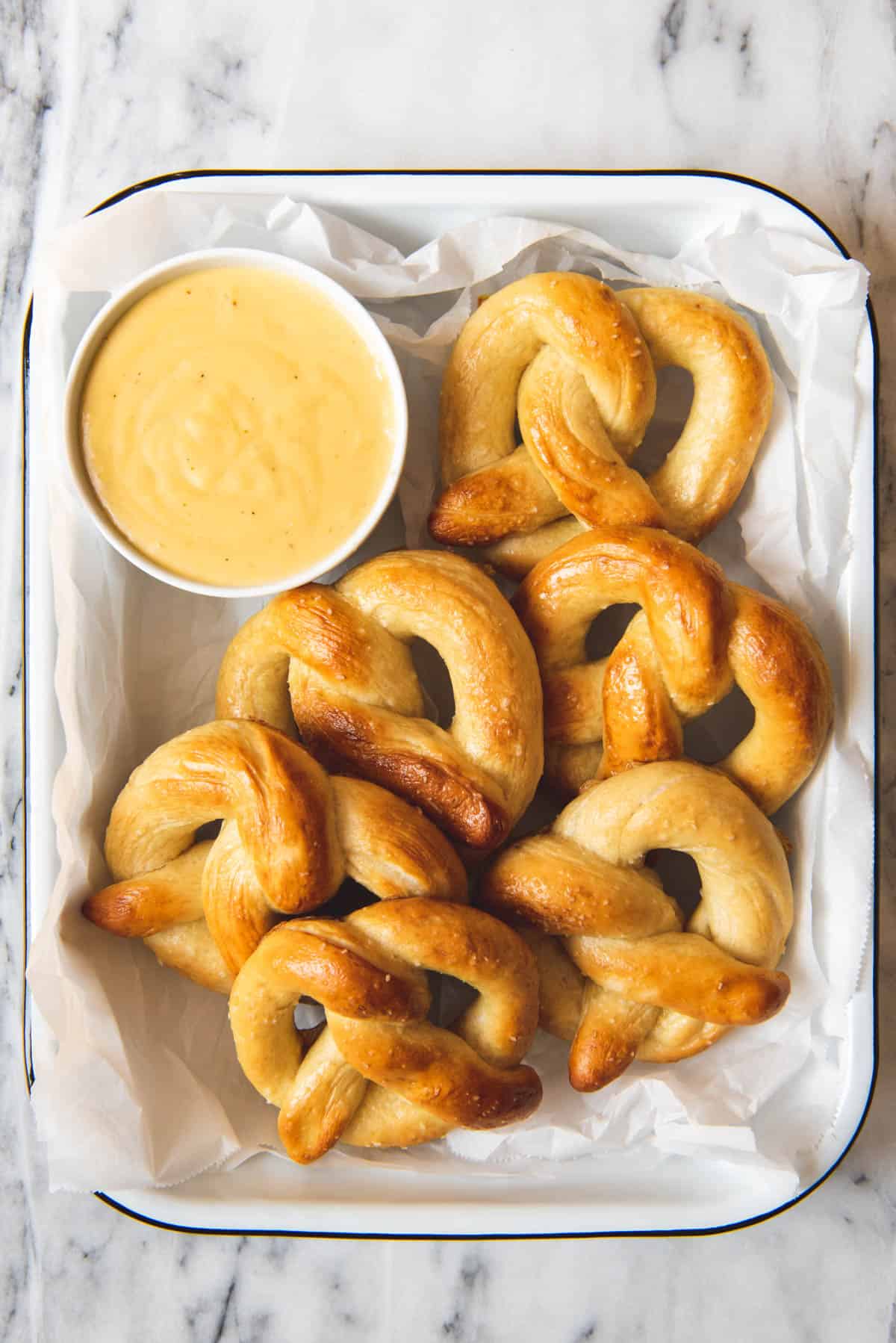 An image of some homemade soft pretzels stacked in a dish with a bowl of mustard cheese dipping sauce on the side.