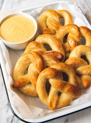 An image of a baking dish filled with golden pretzels and a bowl of mustard cheese dip.