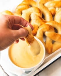An image of dipping a piece of pretzel in mustard cheese sauce.
