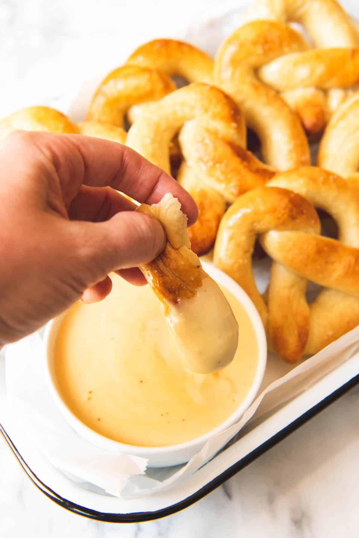 An image of dipping a piece of pretzel in mustard cheese sauce.