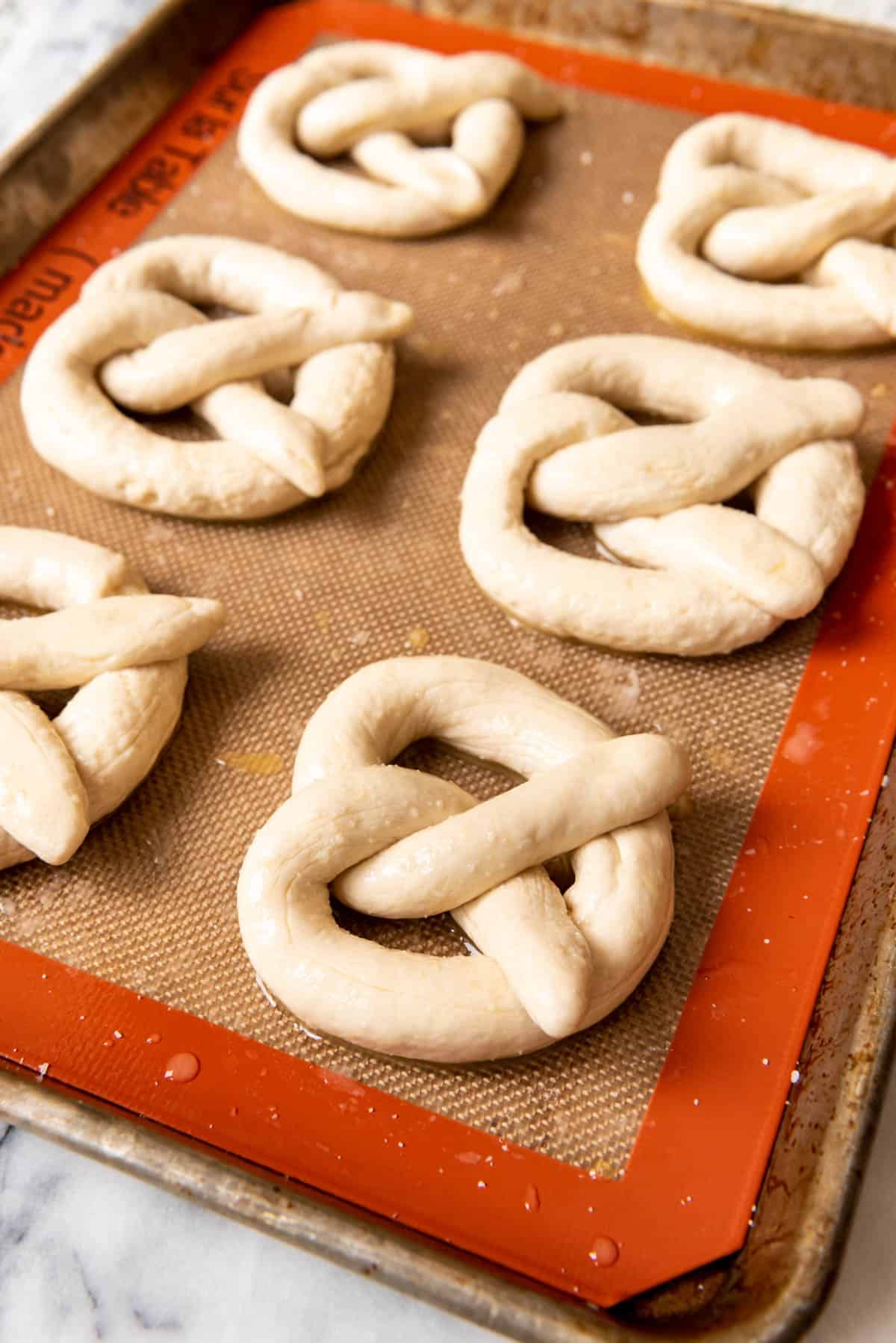 6 pretzels on a baking sheet sprinkled with course salt.