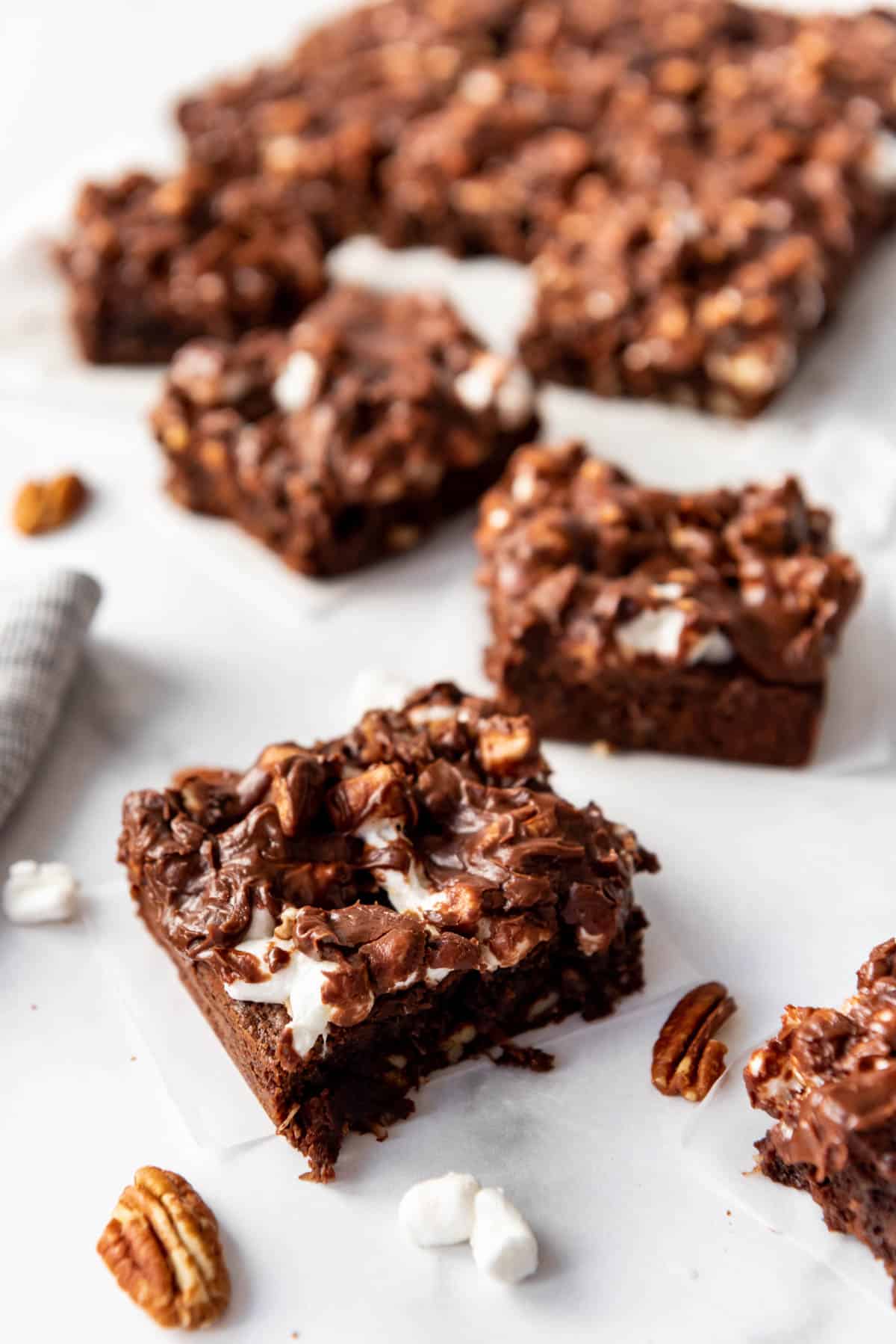 Mississippi mud brownie squares next to scattered marshmallows and pecans.