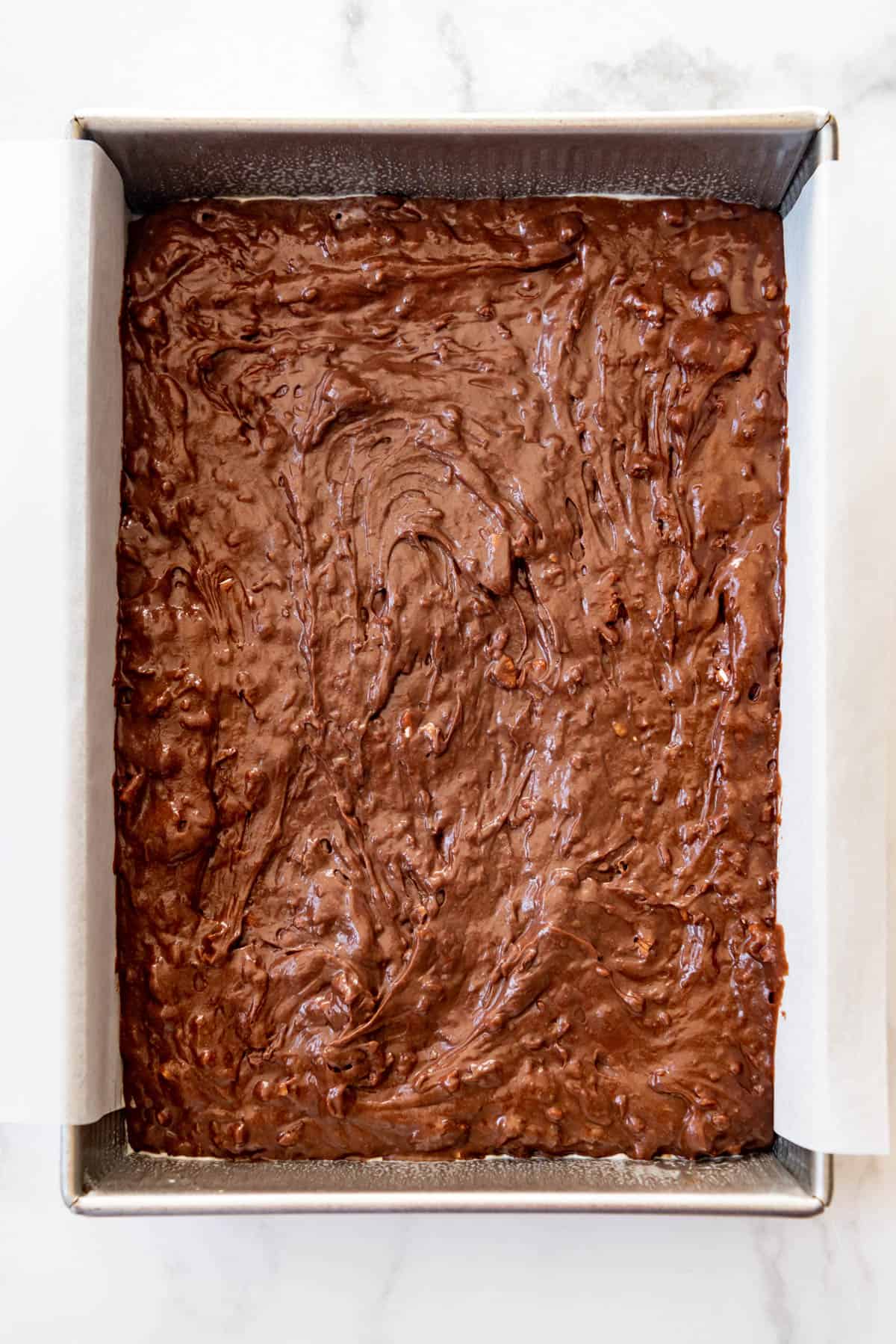 Brownie batter spread in a 9x13-inch pan with a parchment paper sling.