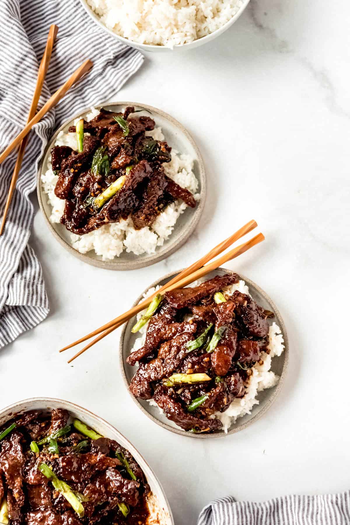 An image of three bowls of Mongolian Beef over rice with chopsticks.