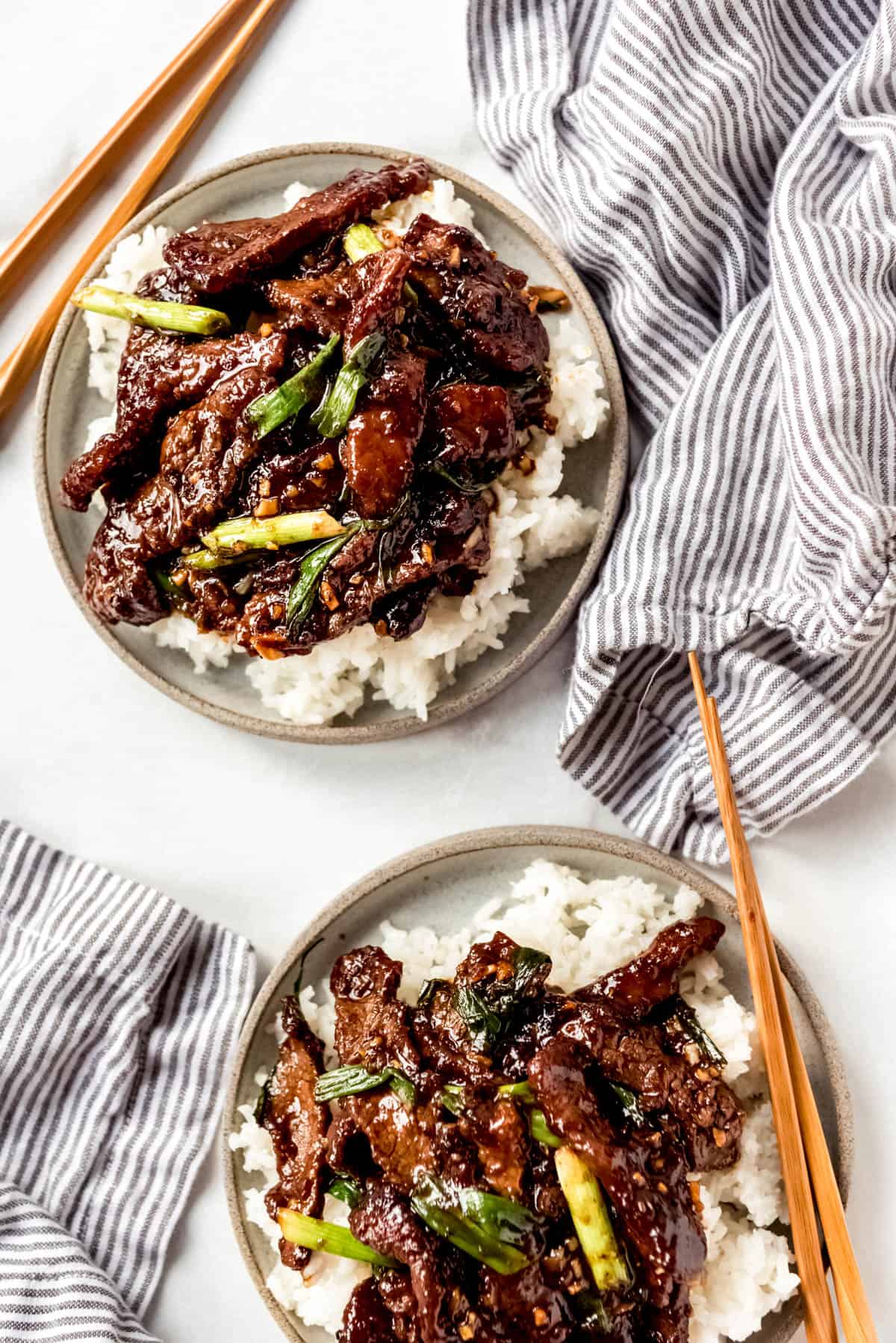 Two bowls of Mongolian Beef on rice with chop sticks.
