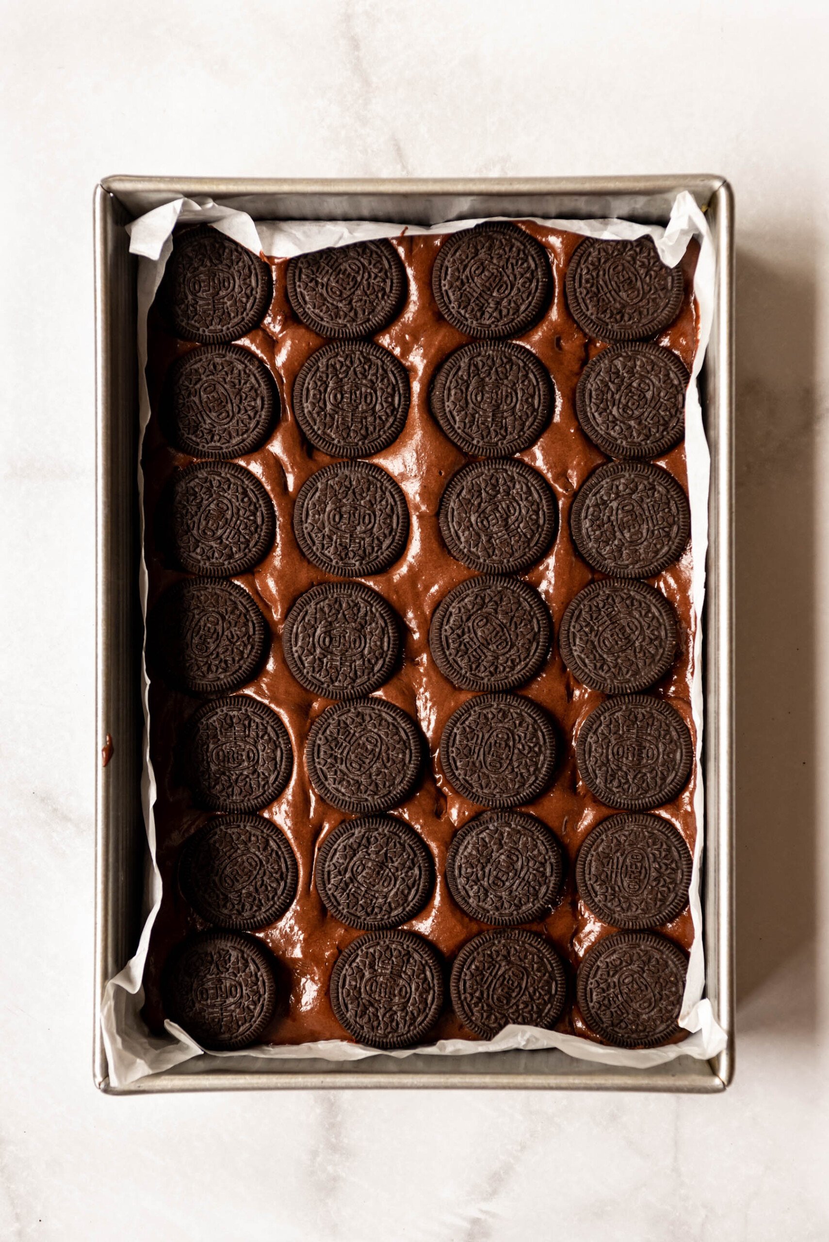 Adding rows of Oreos to a baking dish filled with brownie batter.