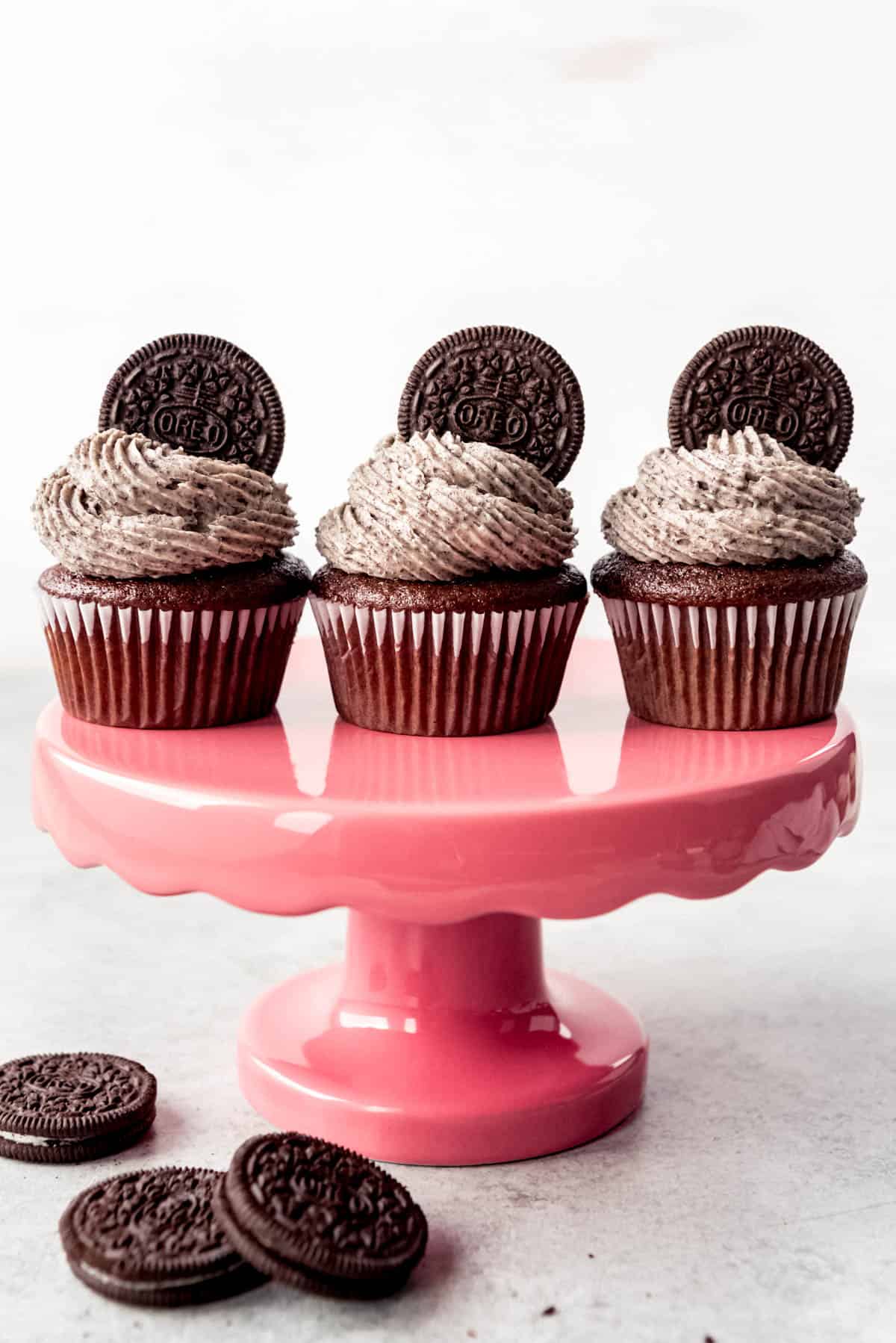 An image of three chocolate cupcakes on a red cake stand with swirls of cookies and cream frosting on top.