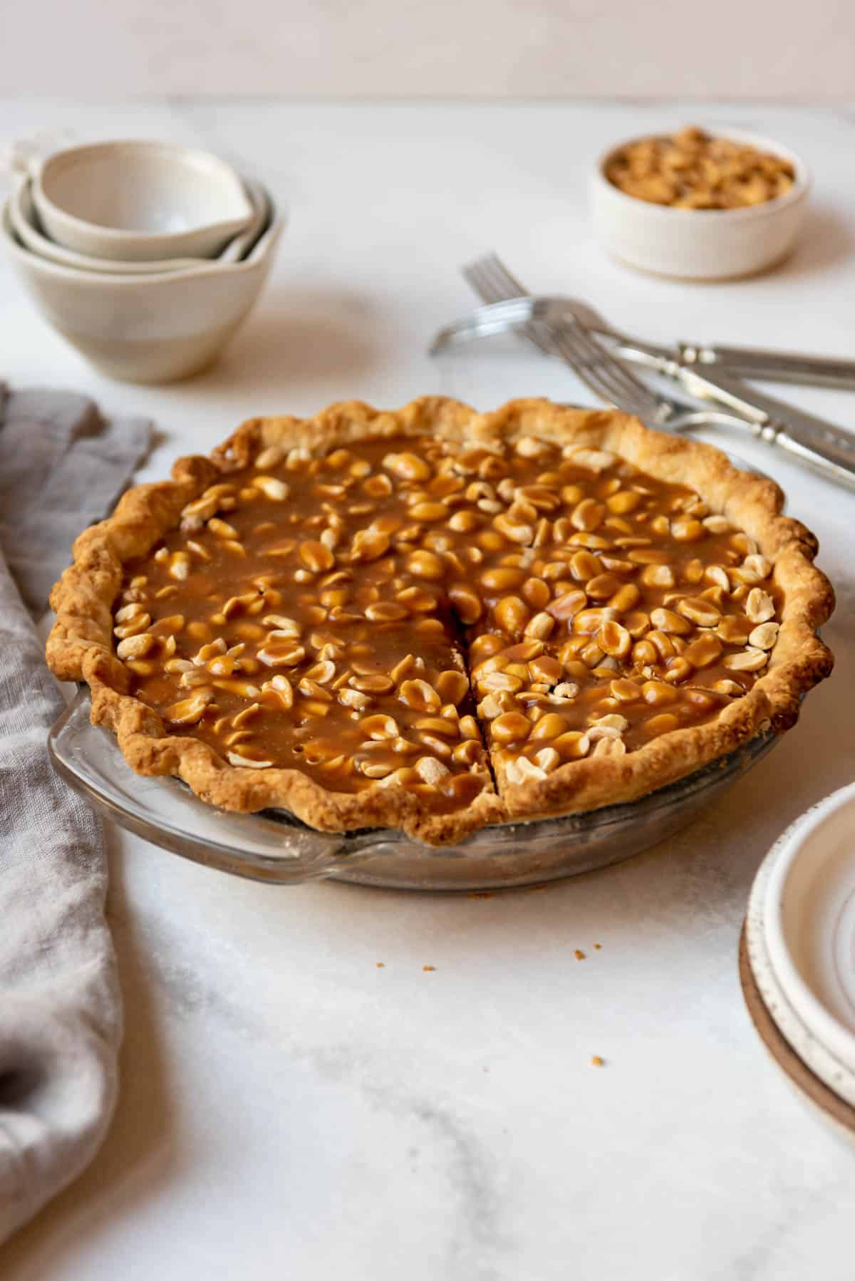 A payday pie with peanuts next to forks, bowls, and a cloth napkin.