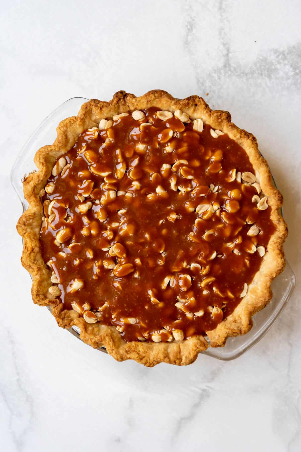 Caramel poured over roasted peanuts in a baked pie crust.