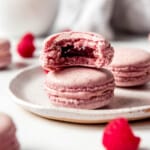 Raspberry Macaron on plate with a bite taken out of it.