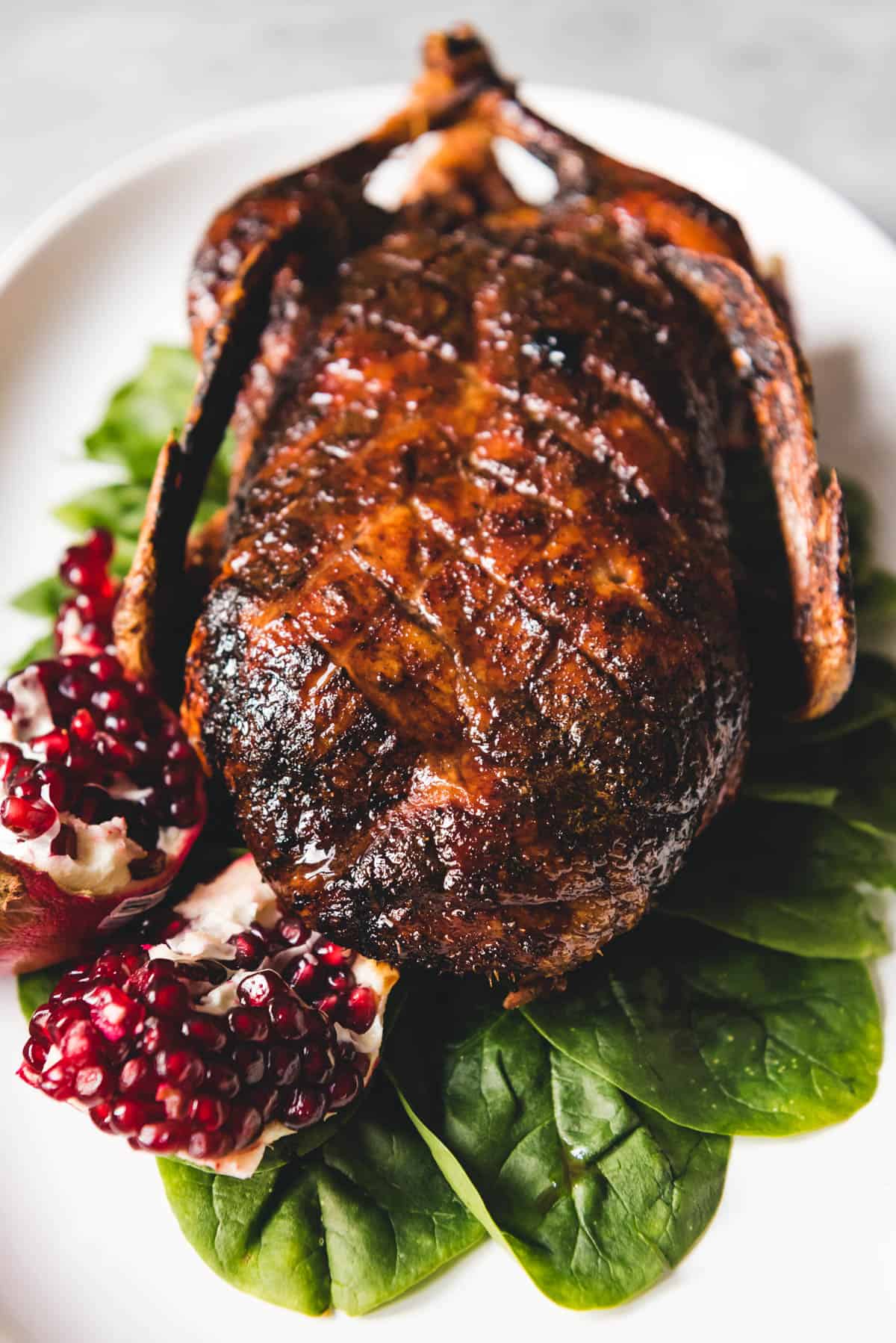 An image of a Honey roasted duck on a bed of spinach with a broken open pomegranate to the side.