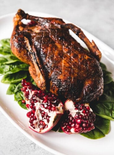 Honey roasted duck on a white platter with spinach and pomegranate.