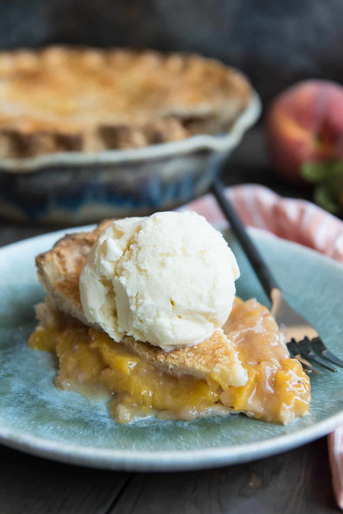 A slice of peach pie on a plate with a scoop of white ice cream on top.