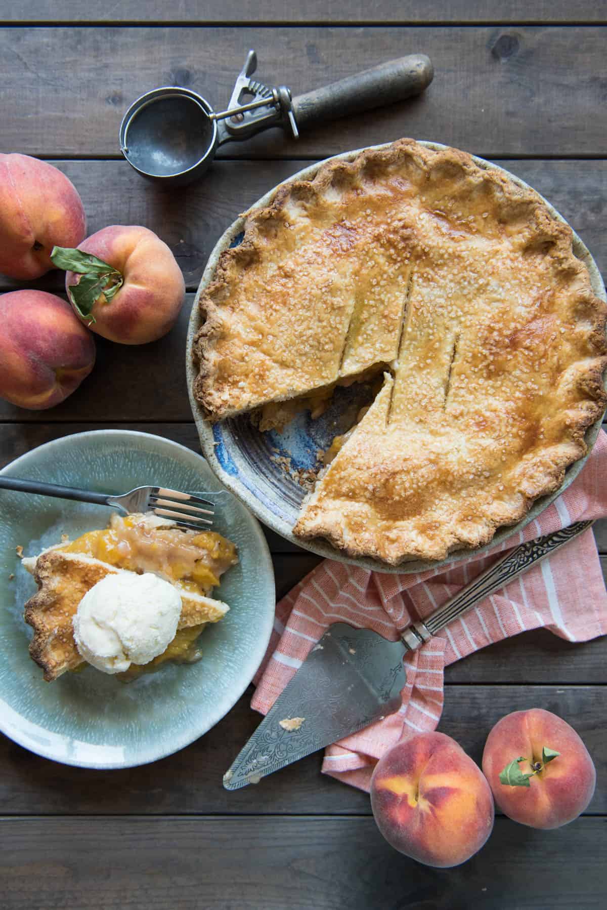 An aerial shot of a peach pie with a slice removed and placed on a plate and then topped with ice cream.